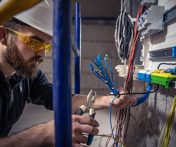 male-electrician-works-switchboard-with-electrical-connecting-cable